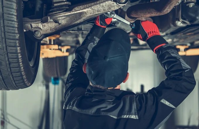 Mechanik w rękawicach roboczych odkręca element zawieszenia pod samochodem uniesionym na podnośniku